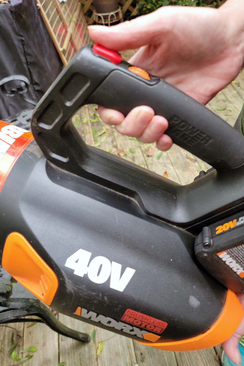 A close up vertical image of the housing of a Worx leaf blower held in two hands by a gardener.