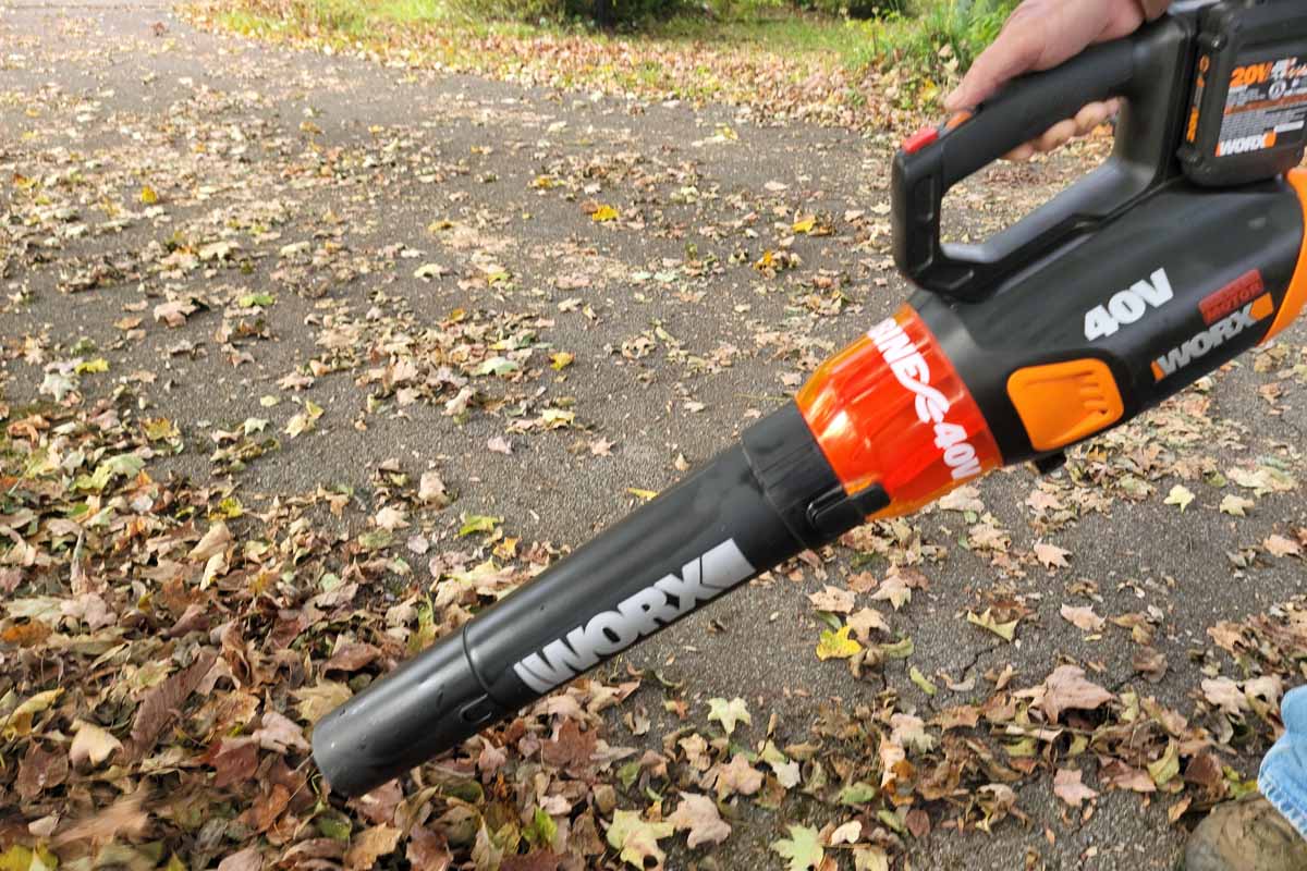 A close up horizontal image of the Worx WG584 40-V Power Share Turbine Cordless Leaf Blower being used to clear leaves from the driveway.