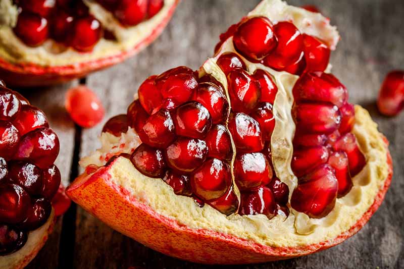 A close up horizontal image of a pomegranate cut into pieces set on a wooden surface.