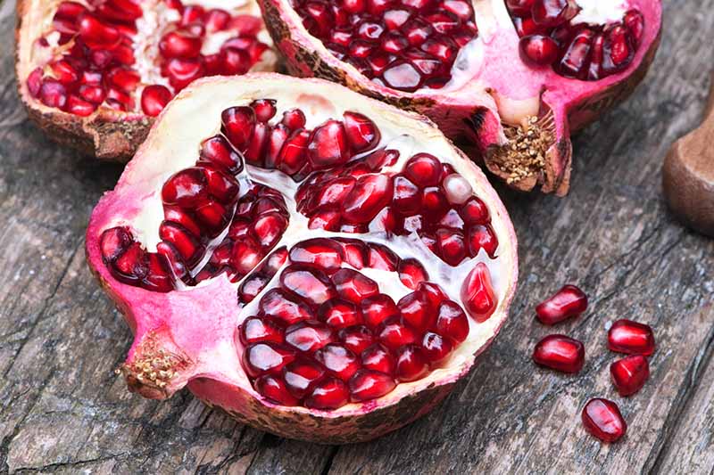 A close up horizontal image of a pomegranate cut in half set on a wooden surface.