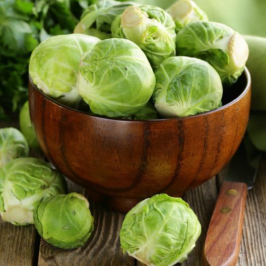 A close up square image of a bowl of 'Long Island Improved' Brussels sprouts set on a wooden surface.