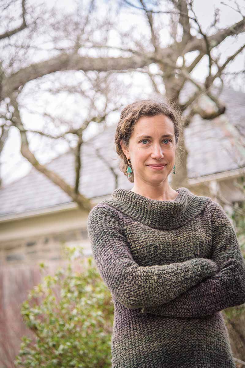 A close up portrait of the author Stephanie Bruneau with a residence in soft focus in the background.