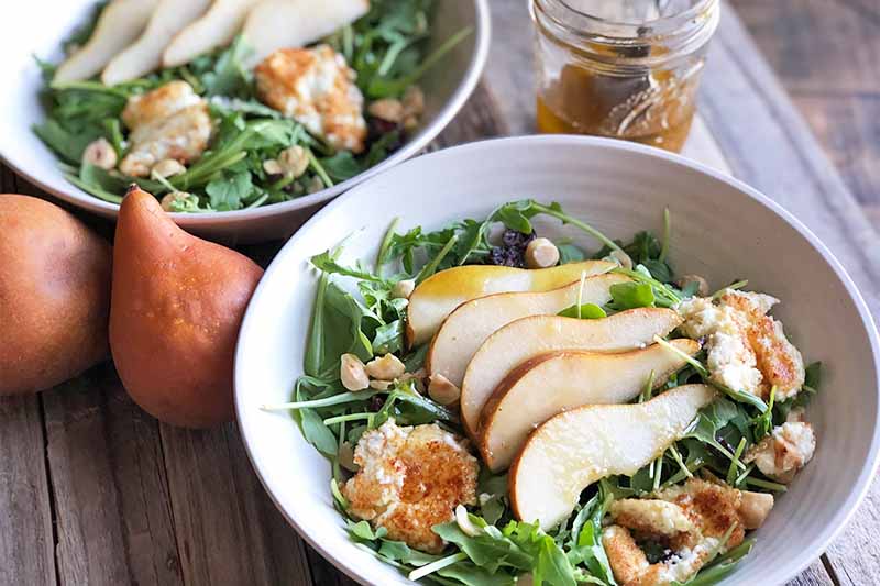 A close up horizontal image of a freshly prepared dish of goat cheese, pear, and arugula salad set on a wooden surface.