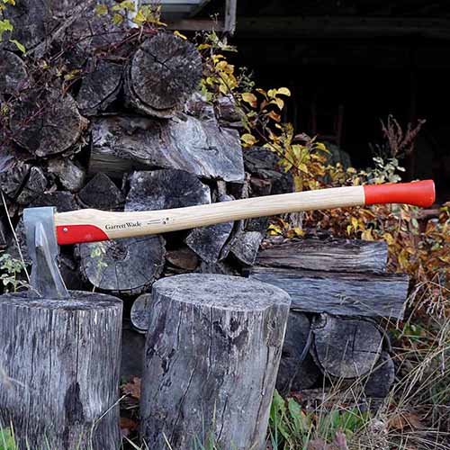 A close up square image of a Garret Wade Professional Maul with a wood pile in soft focus in the background.