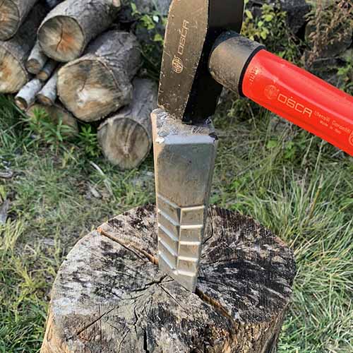 A close up square image of a wood splitting wedge being driven into a piece of wood by a splitting maul.