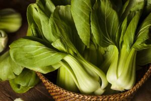A close up horizontal image of bok choy in a wicker basket.
