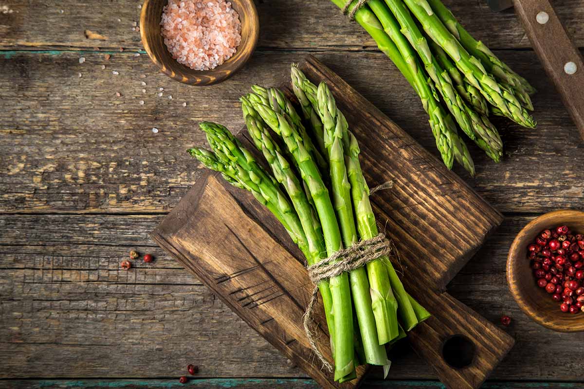 A close up horizontal image of bunches of asparagus spears tied together with string set on a wooden chopping board.