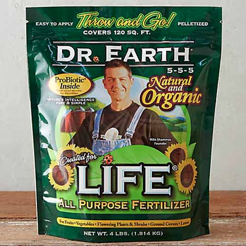 A close up square image of a bag of Dr Earth Natural and Organic All Purpose Fertilizer set on a wooden surface.