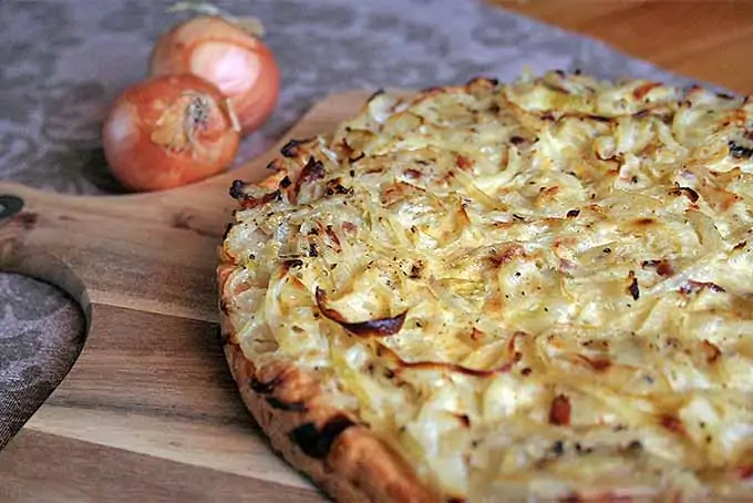 A close up horizontal image of a freshly baked German onion tart set on a wooden chopping board.