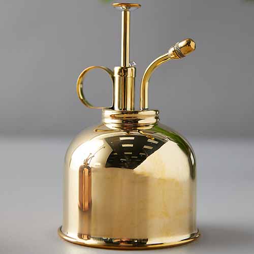 A close up square image of a brass misting bottle isolated on a gray background.