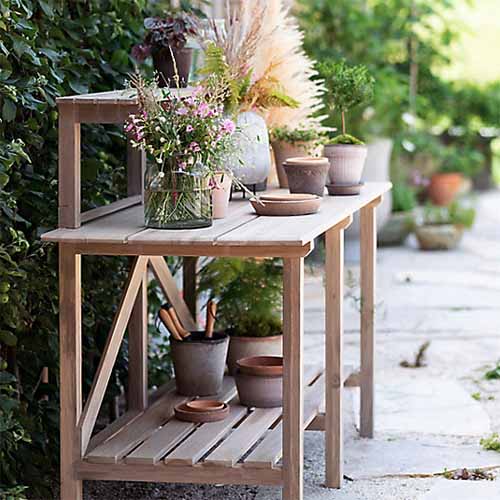 A close up square image of a wooden potting table set outside in the garden.
