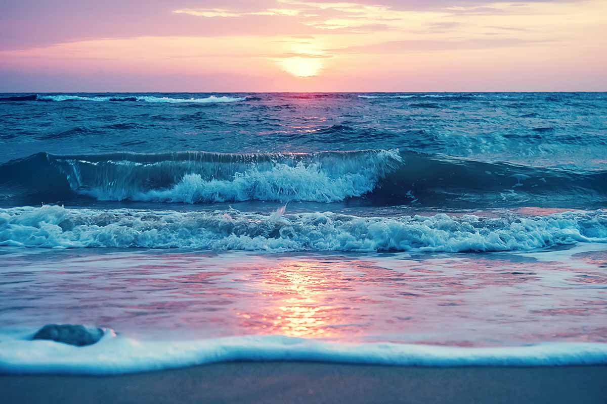 A horizontal image of sunrise as viewed from a beach across the sea.
