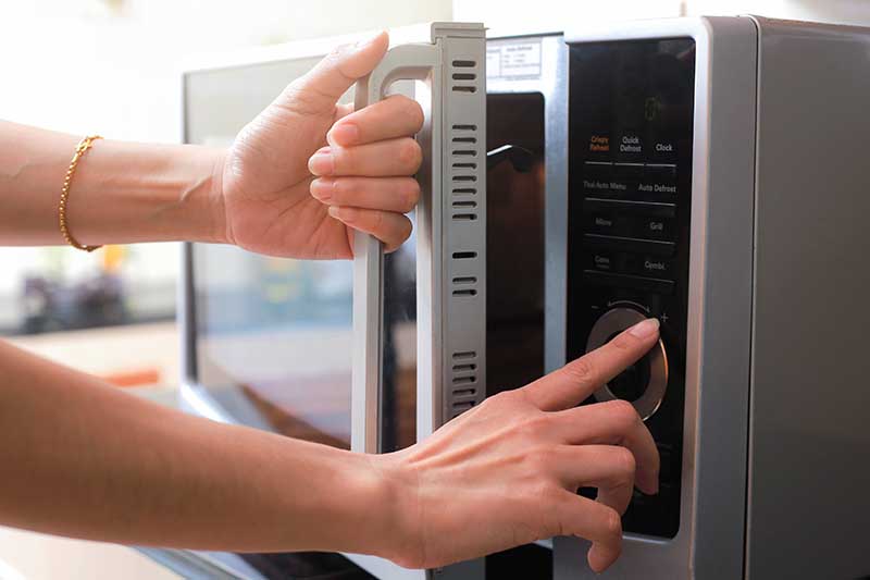 A close up horizontal image of a woman opening a door of a microwave oven.