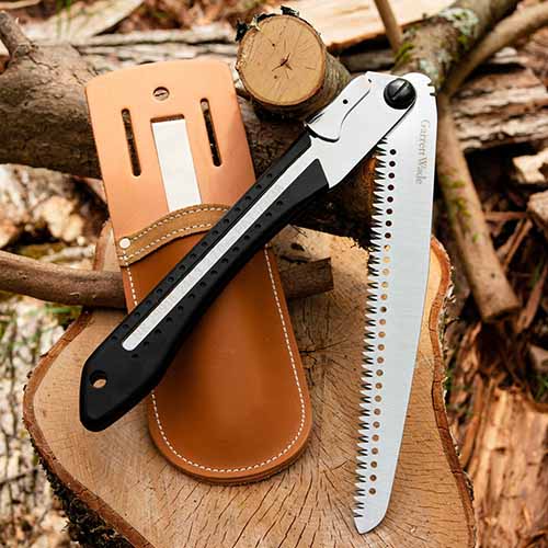 A close up square image of a folding pruning saw with a leather holster set on a piece of wood.