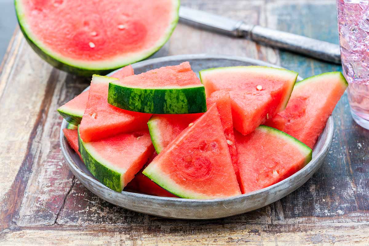 A close up horizontal image of a plate of sliced fresh watermelon set on a wooden surface.