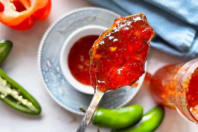 A close up horizontal image of a spoonful of freshly homemade hot pepper jelly.