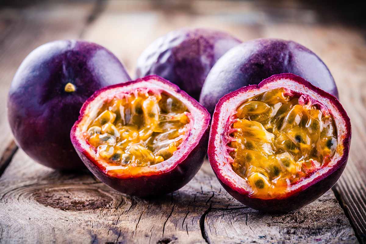 A close up horizontal image of ripe passion fruits whole and cut in half set on a wooden surface.