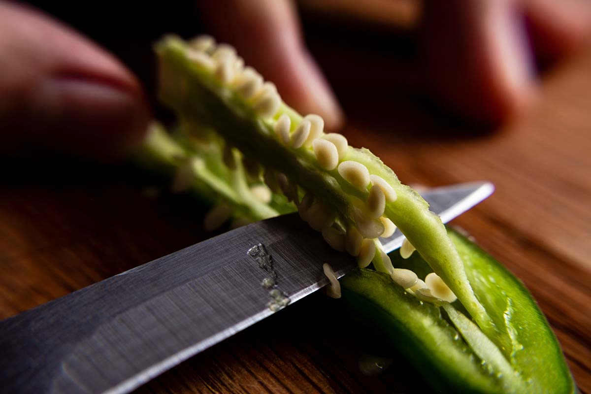 A close up horizontal image of a knife cutting the placenta from a serrano pepper.