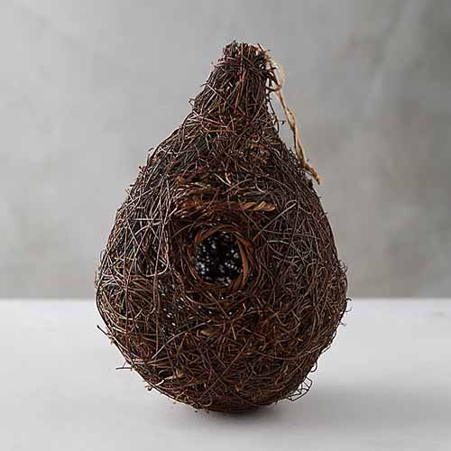 A close up square image of a decorative bird's nest set on a white surface.