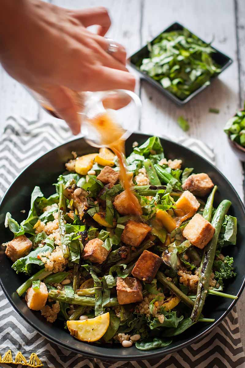 A close up vertical image of a freshly prepared fried tofu with charred green bean salad in a black bowl.