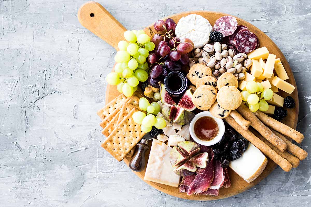 A top down horizontal image of a cheeseboard with a variety of different fruits, nuts, and breads.