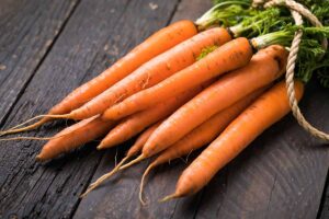 A close up horizontal image of freshly harvested carrots set on a wooden surface.