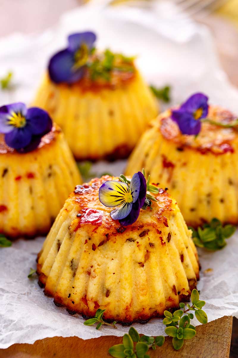 A close up vertical image of cupcakes fresh from the oven decorated with edible pansies.