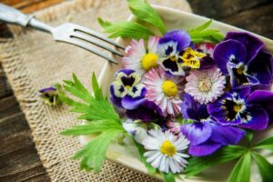 A close up horizontal image of a plate filled with freshly harvested edible flowers set on a wooden table.