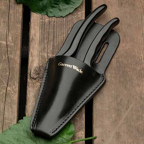 A close up square image of a black leather sheath for pruning shears set on a wooden surface.