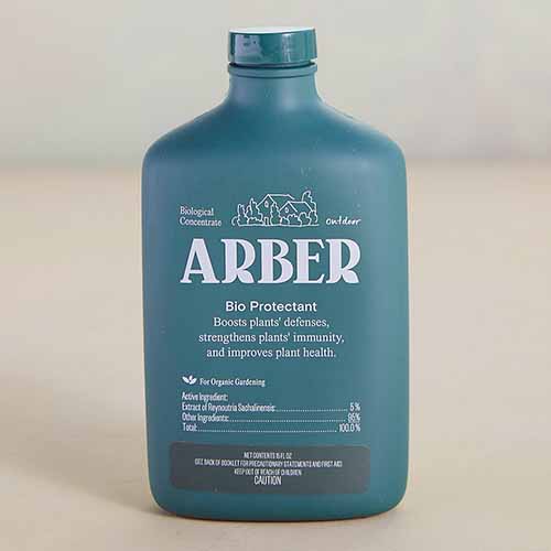 A close up of a bottle of Arber Bioprotectant isolated on a light brown background.