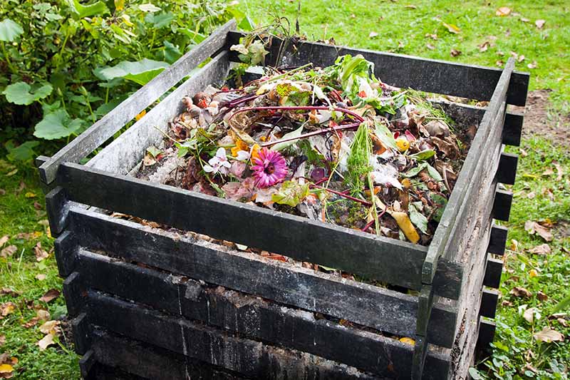A close up horizontal image of a compost pile in a wooden container.