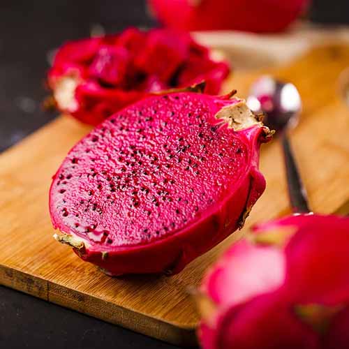 A close up square image of 'American Beauty' pitaya cut in half and set on a wooden surface.