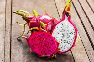 A close up horizontal image of dragon fruits cut in half and set on a wooden surface.