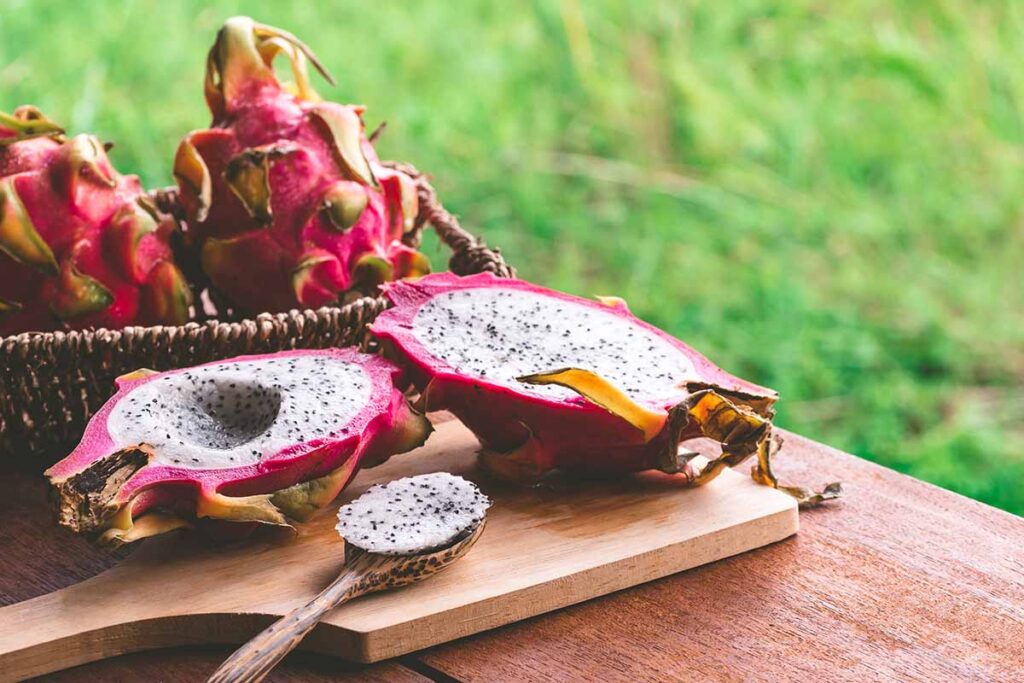A close up horizontal image of a dragon fruit cut in half and set on a wooden surface.