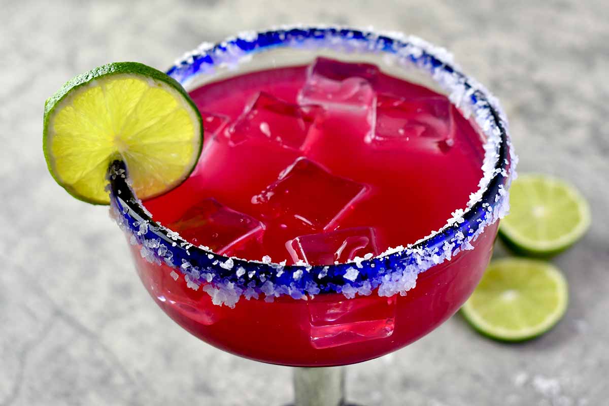 A close up horizontal image of a margarita cocktail garnished with lime set on a gray surface.