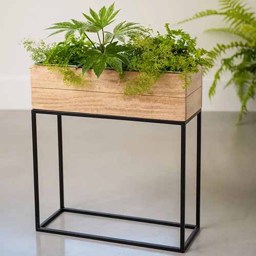 A square image of a wooden elevated rectangular planter set on a concrete floor.