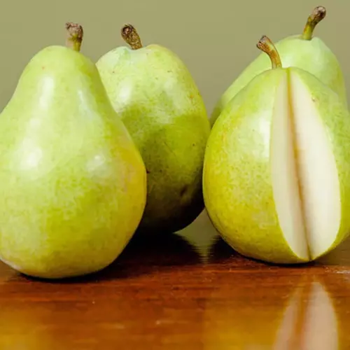 A close up of whole and sliced 'Hood' pears set on a wooden surface.