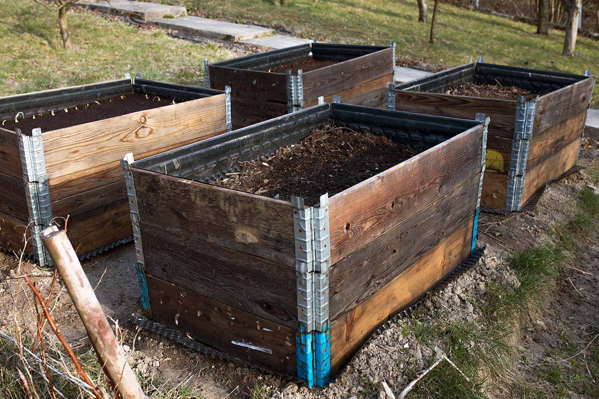 A horizontal image of raised garden beds constructed from wood and bits of metal set on the ground in the garden.
