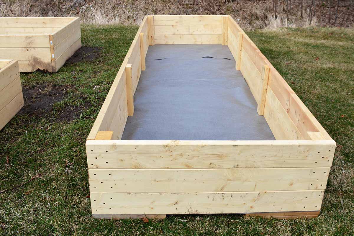 A horizontal image of a newly constructed wooden raised garden bed with landscape fabric in the bottom.