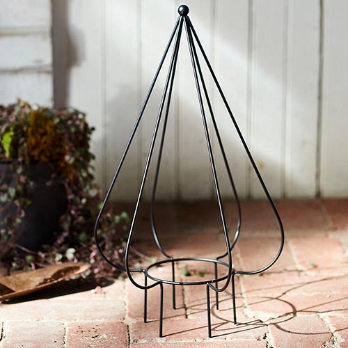 A square image of an iron topiary frame to be used to support vining plants set on a brick surface.