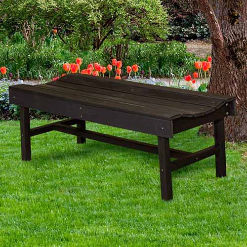 A square image of the Little Cottage Company Classic Vineyard Bench in Tudor Brown set on the lawn under a tree with tulips in the background.