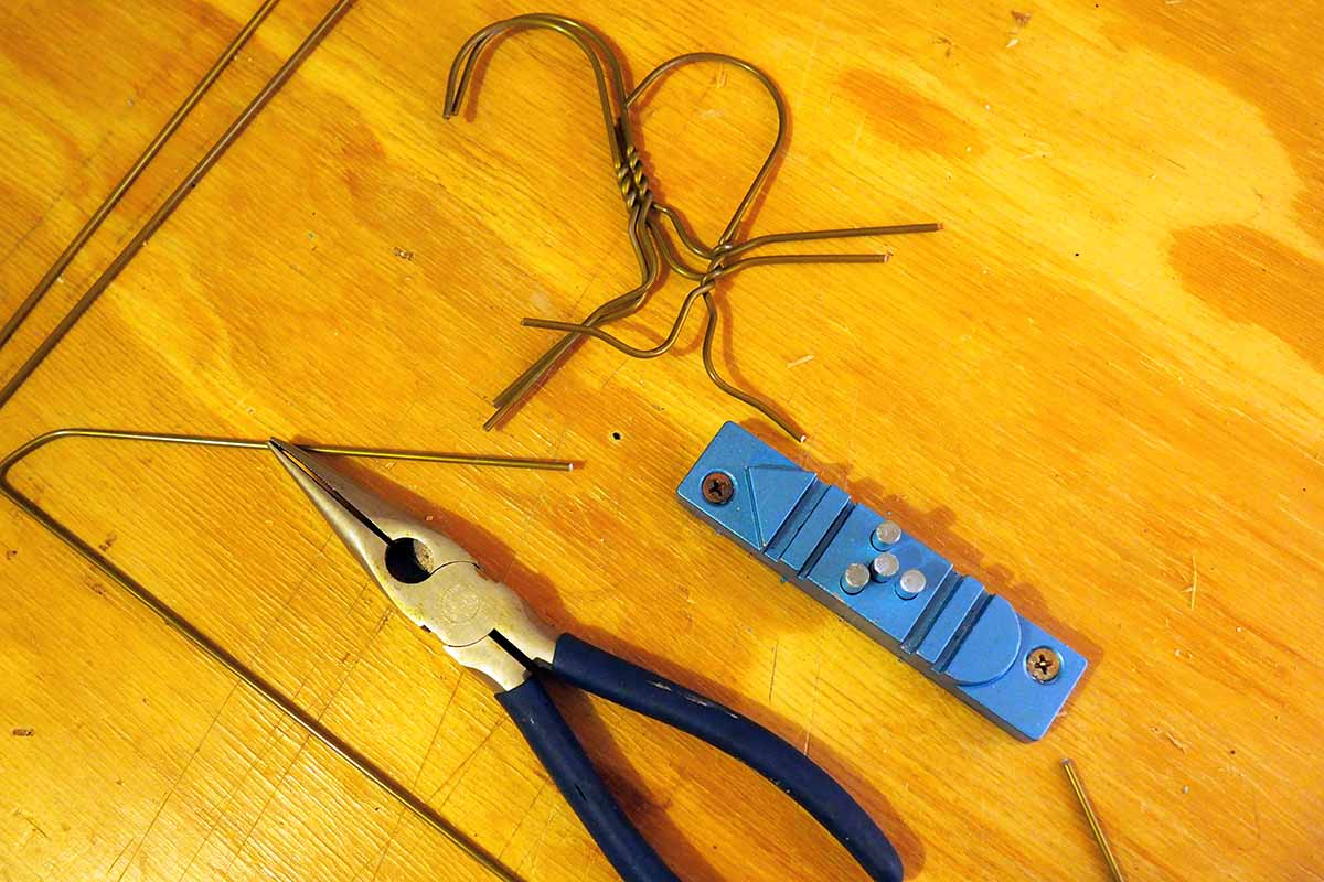 A close up horizontal image of a wire coat hanger cut into pieces for fashioning a flower support, set on a wooden surface with a pair of pliers.
