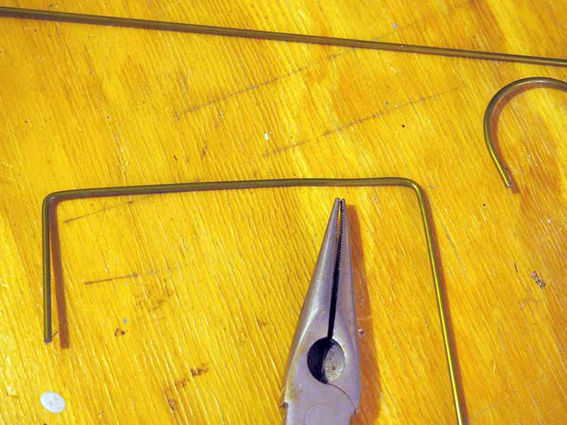 A close up horizontal image of a pair of pliers and metal pieces set on a wooden surface.