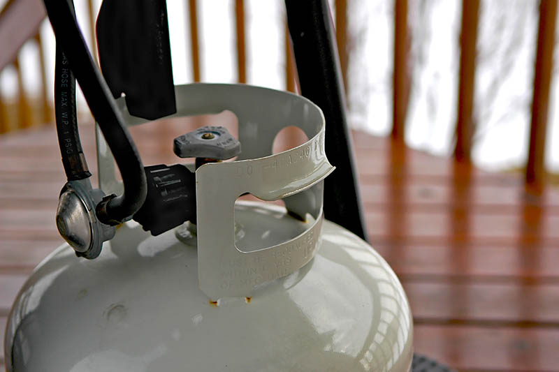 A close up horizontal image of a propane tank and connector.