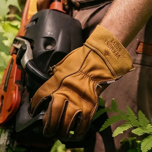 A square image of a gardener wearing The Vermonter leather gloves while operating some heavy machinery.