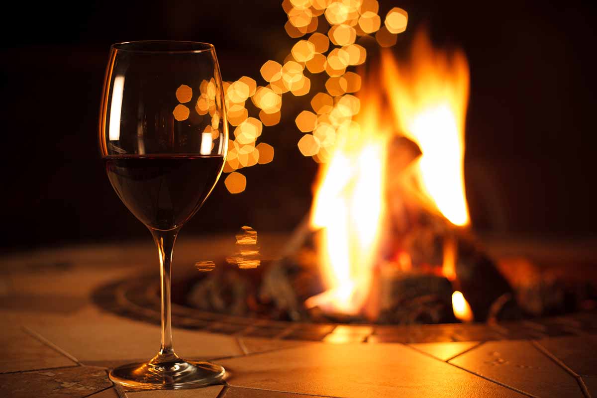 A close up horizontal image of a wine glass in front of a decorative outdoor firepit.