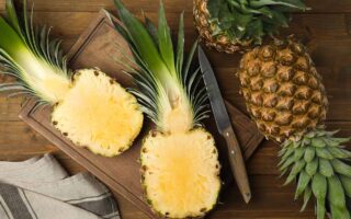 A close up horizontal image of whole and sliced pineapples set on a wooden surface.