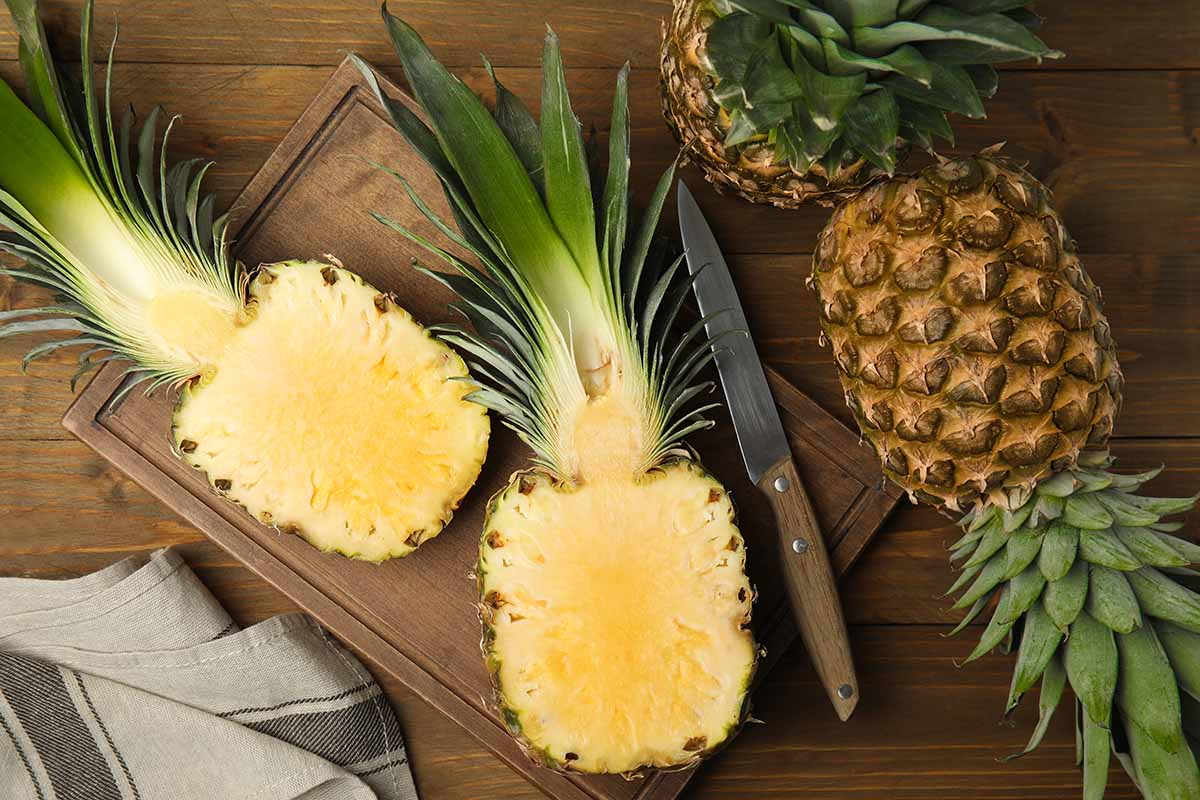 A close up horizontal image of whole and sliced pineapples set on a wooden surface.