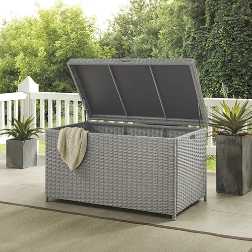 A square image of the Rosecliff Heights Wicker Box in gray set outdoors on a covered patio with the lid open.