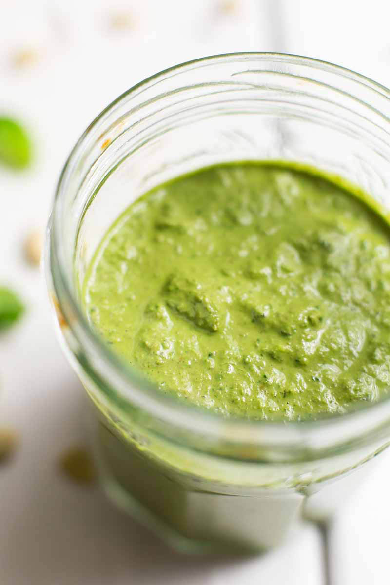 A close up vertical image of a glass jar filled with freshly-prepared pesto.